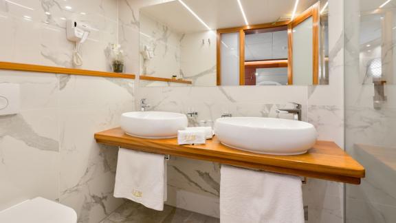 A bright bathroom with white marble, oval washbasin and large mirror on the wall.